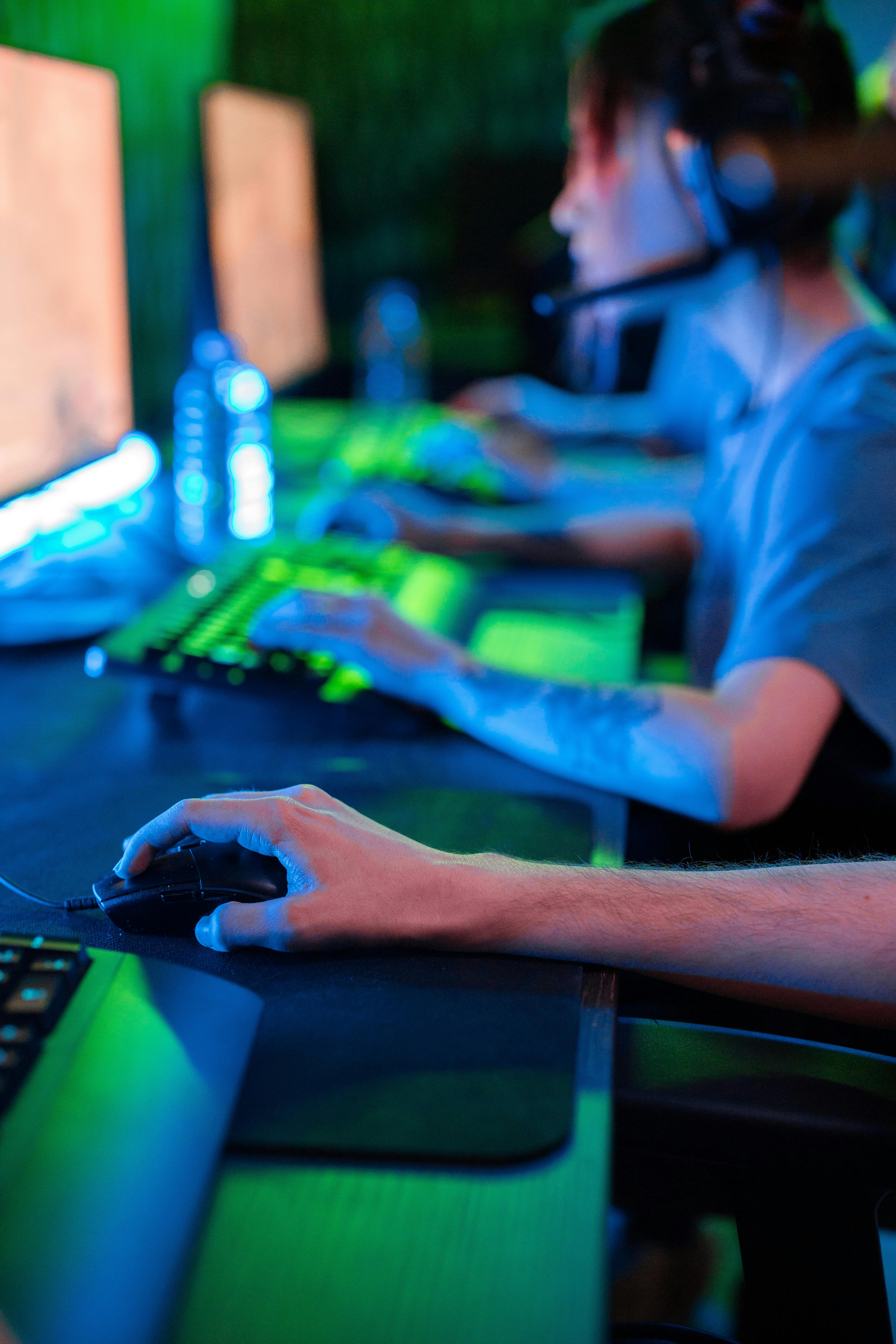 Nahaufnahme einer Person an einem beleuchteten Gaming-Setup mit Tastatur und Monitor.