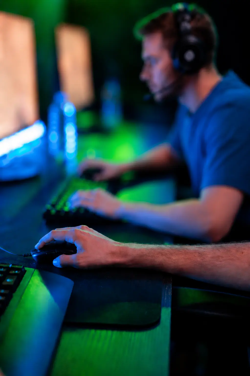 Nahaufnahme einer Person an einem beleuchteten Gaming-Setup mit Tastatur und Monitor.