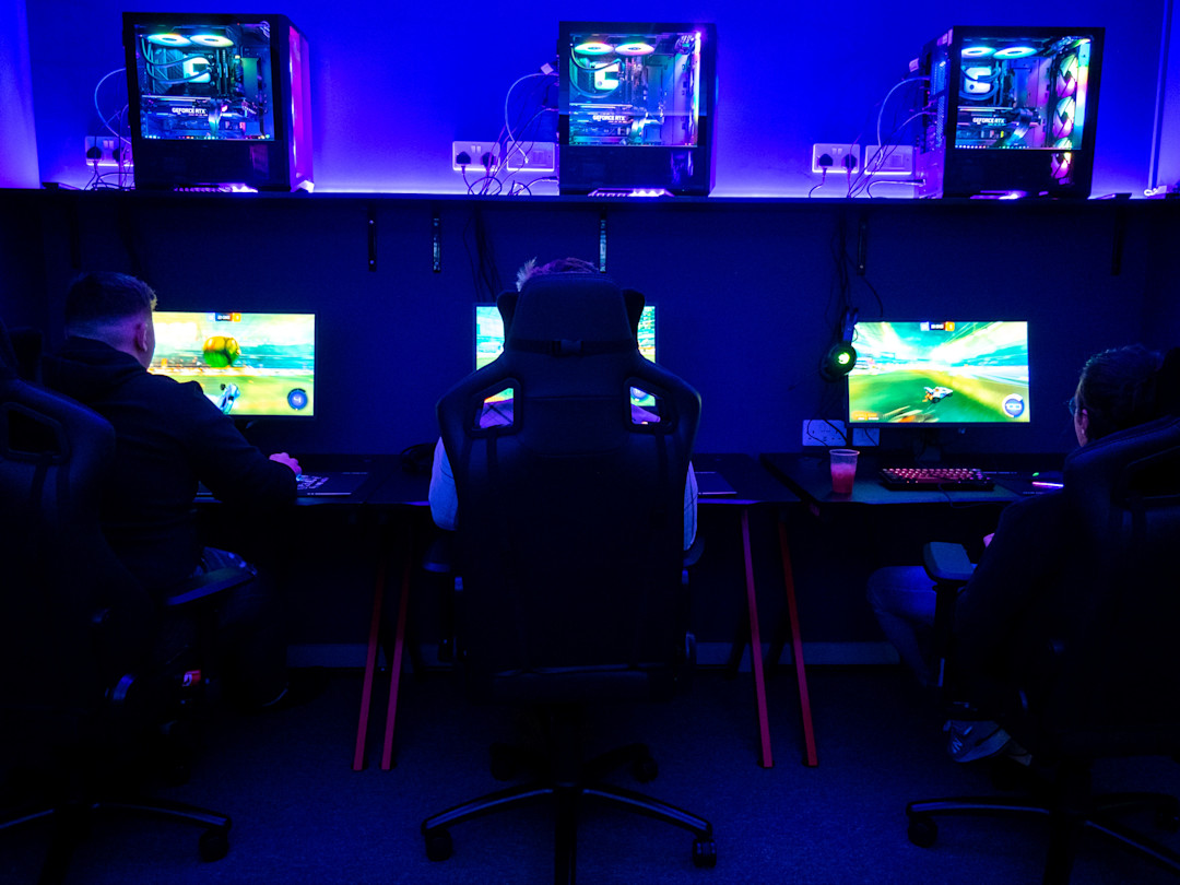 Gaming-Raum mit mehreren vorbereiteten Setups, Monitoren und Stühlen.