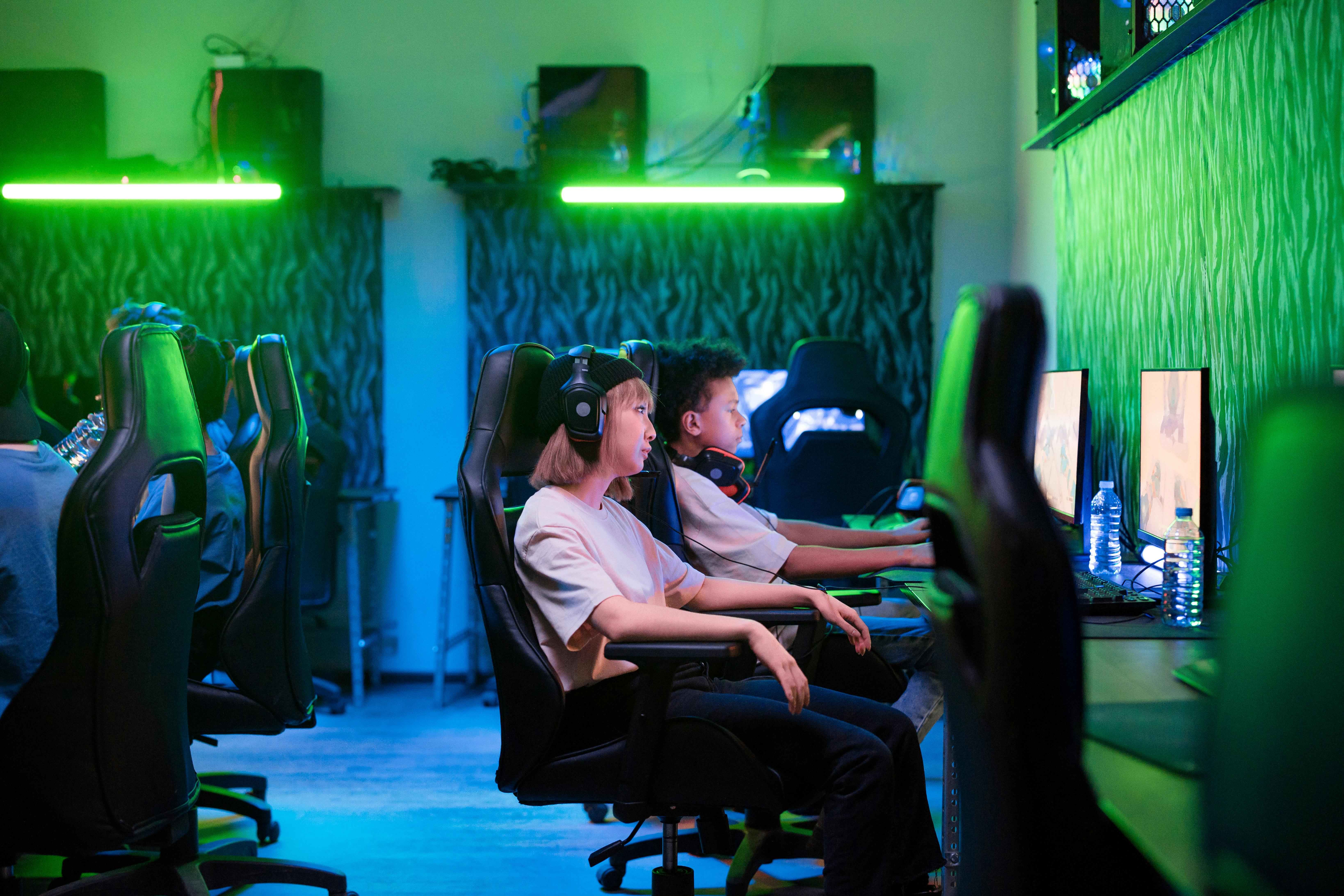 Mehrere Personen an vorbereiteten Gaming-Setups mit Monitoren und Headsets.
