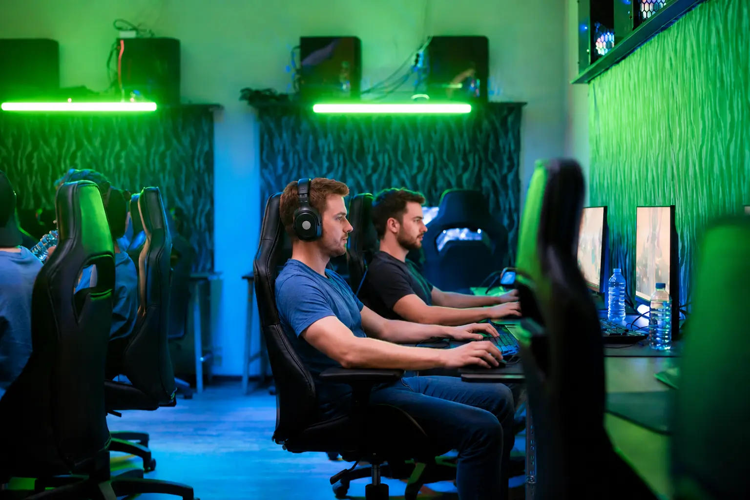 Mehrere vorbereitete Gaming-Setups mit Monitoren, Stühlen und Beleuchtung.